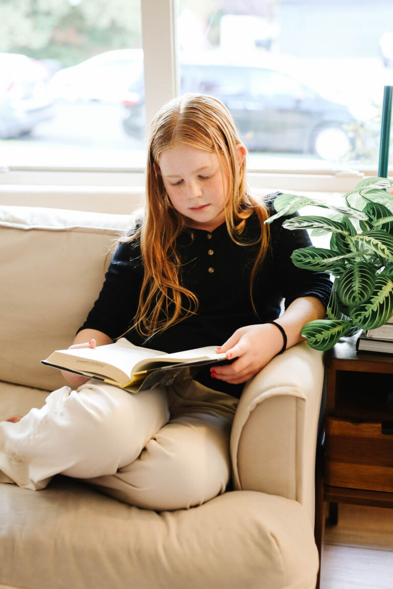 middle school girl with read hair reading a book on a couch